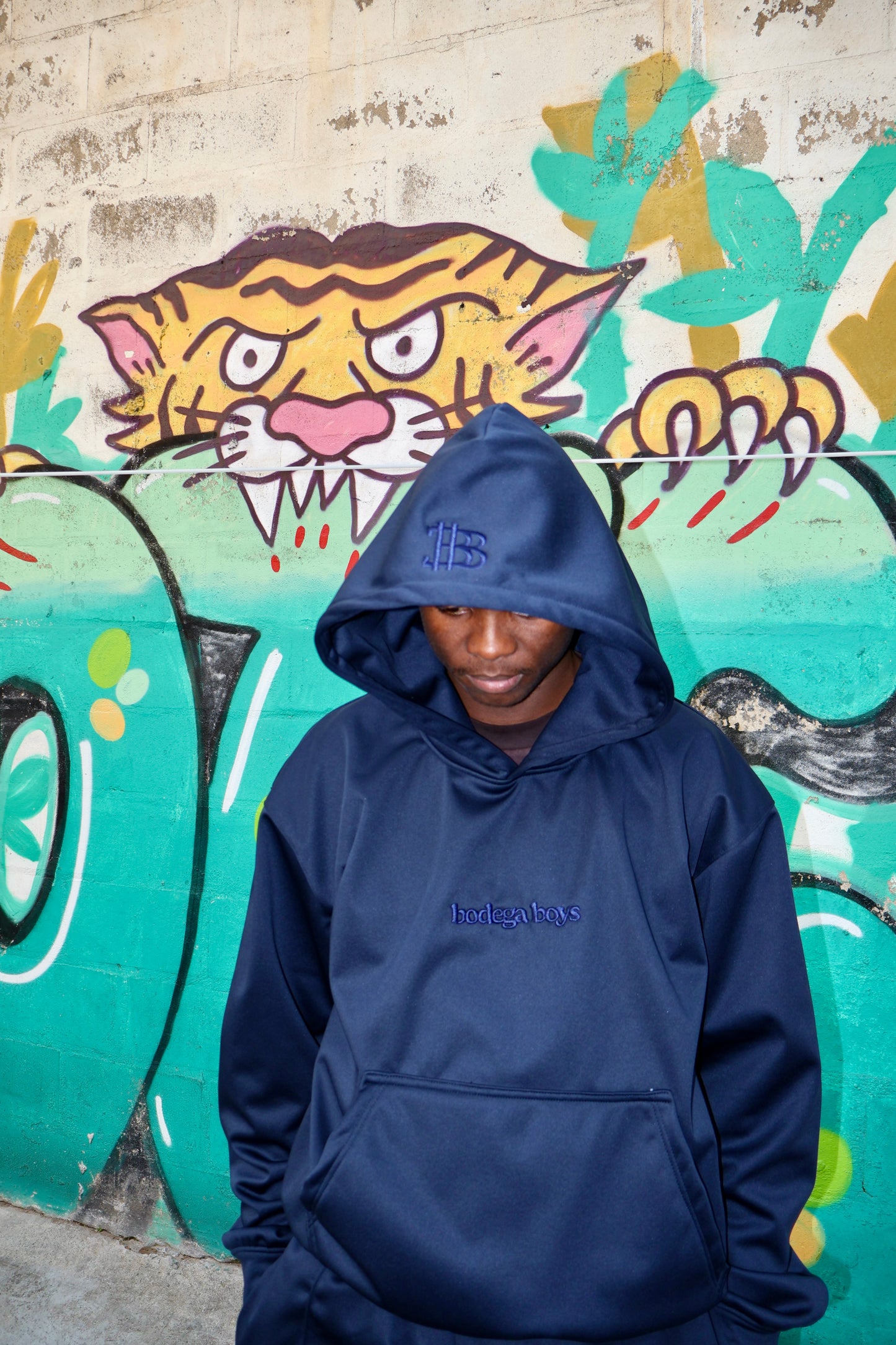 Person wearing a navy blue hoodie with a brand logo in front of a colorful mural.